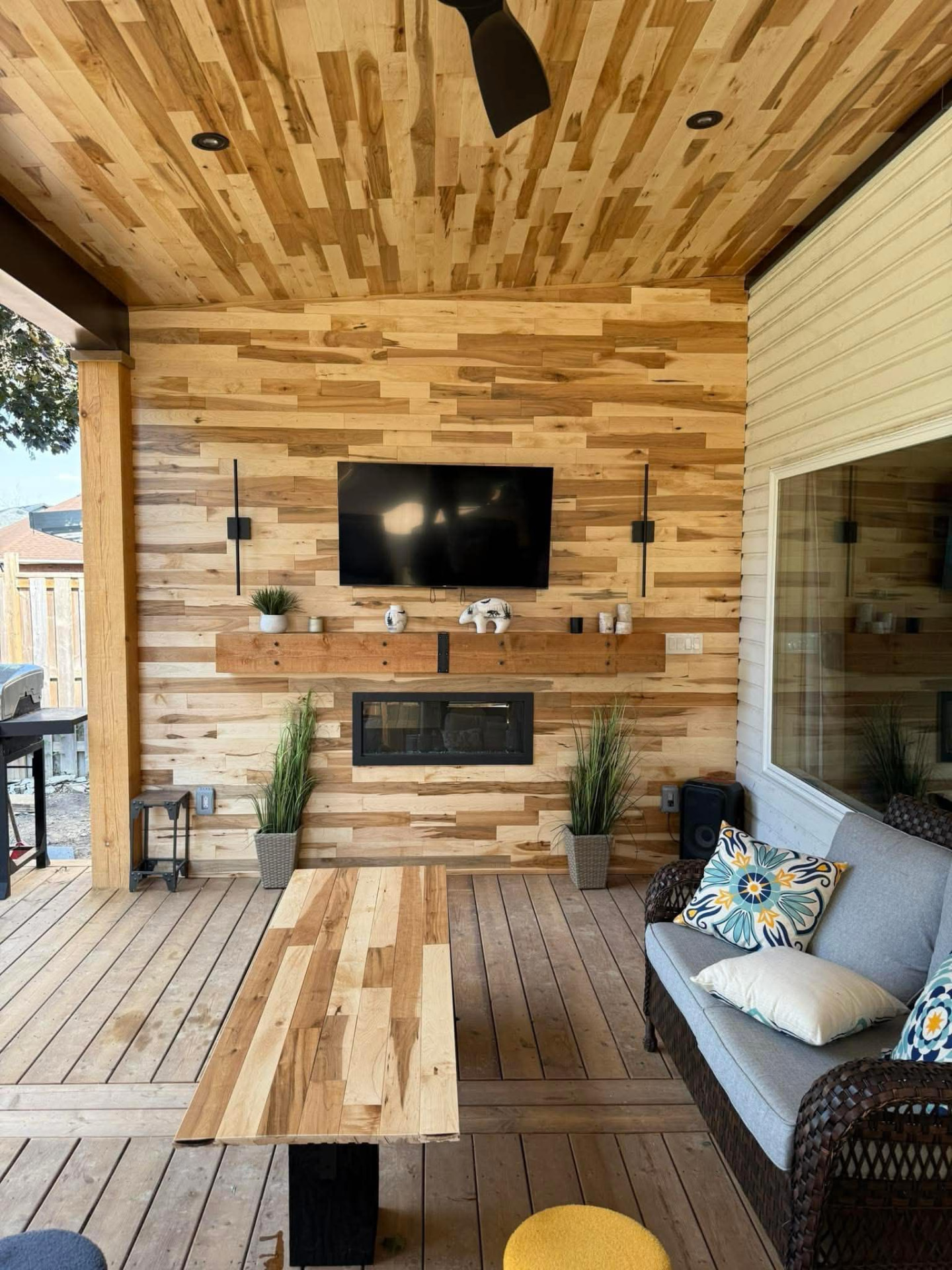 Completed covered patio with a custom wood feature wall, fireplace, and television